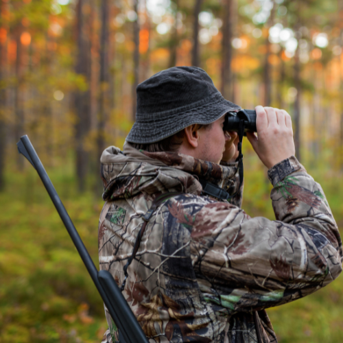 Hunter looking through binoculars in the woods